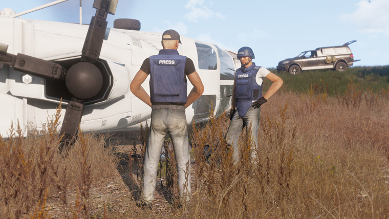 Two men with press vests stand next to a crashed helicopter.